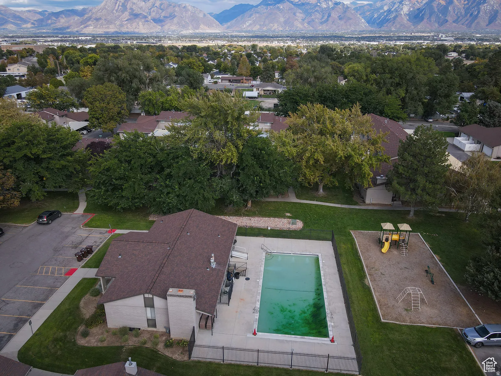 Outdoor swimming pool, adjacent playground, expansive green spaces, mature trees, and mountain backdrop