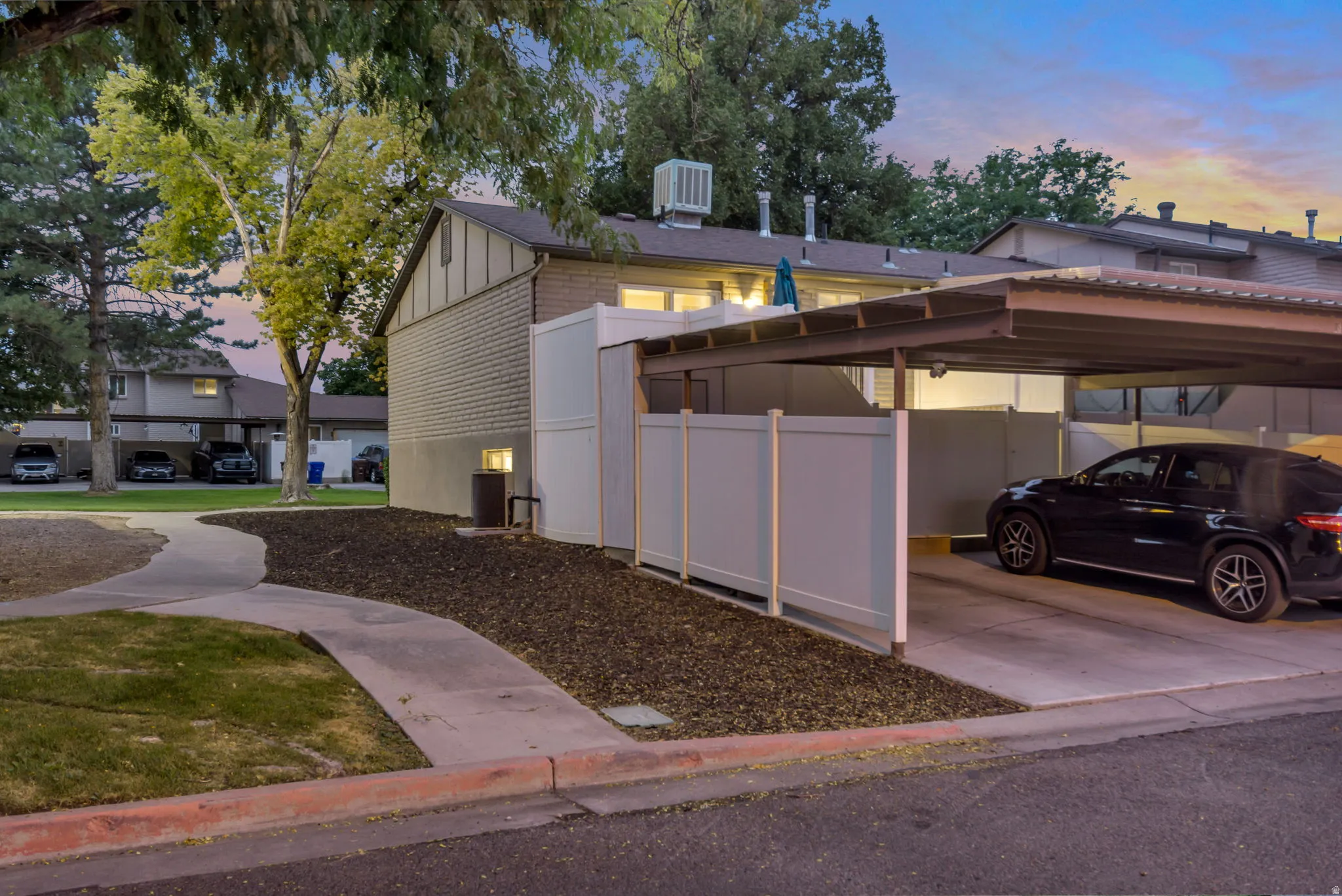 Carport parking with a metal roof and concrete pad, complemented by a privacy fence and a paved pathway