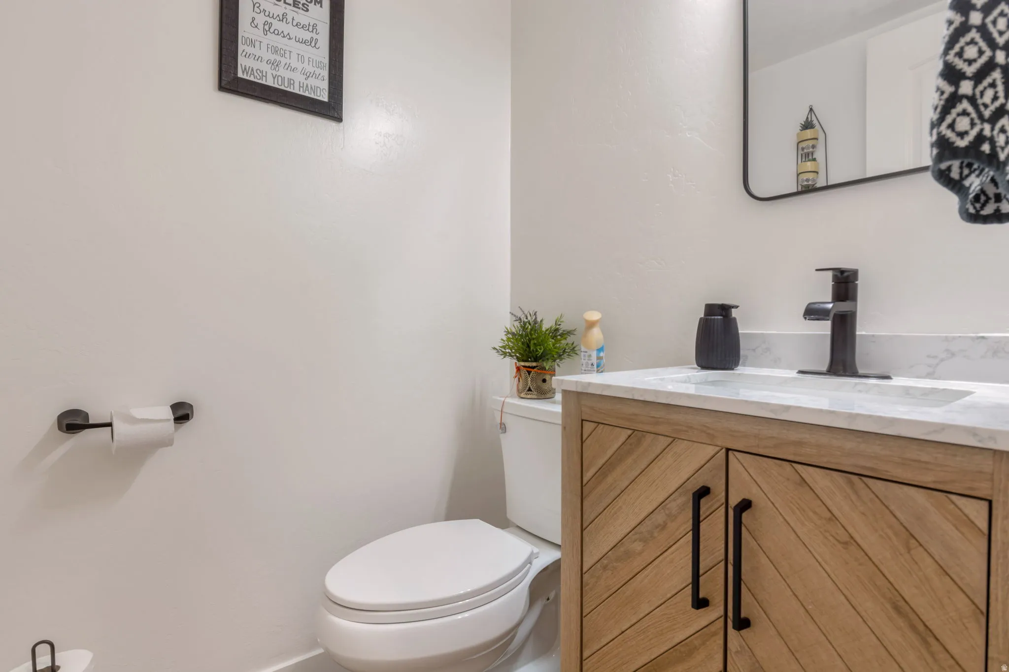 Modern vanity with a rectangular basin, black hardware, wood-finish cabinetry, and a stone-finish countertop