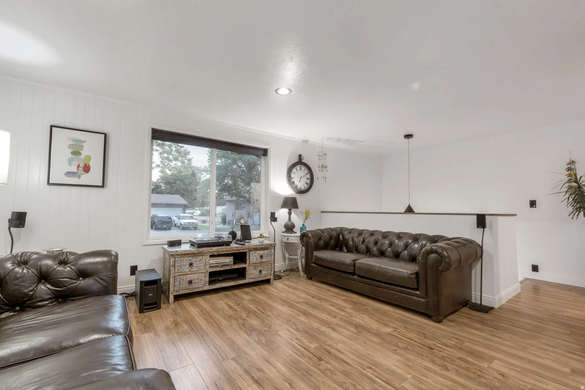 Living area featuring wood-finish flooring, white paneling, white walls, a large window, and recessed lighting
