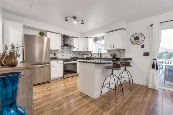 Wood-finish flooring throughout, stainless steel appliances, white cabinetry with dark hardware, black speckled backsplash, and a sliding glass door to an outdoor area