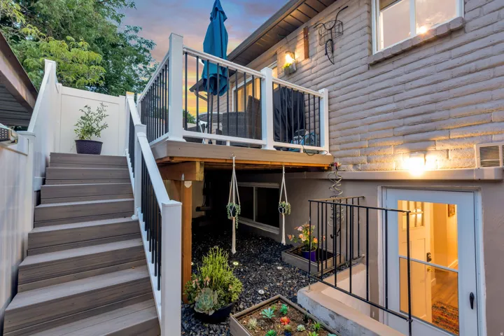 Exterior featuring a raised deck with white railings and black balusters, a staircase with composite treads, a lower patio area with black gravel, and a white exterior door with glass panels