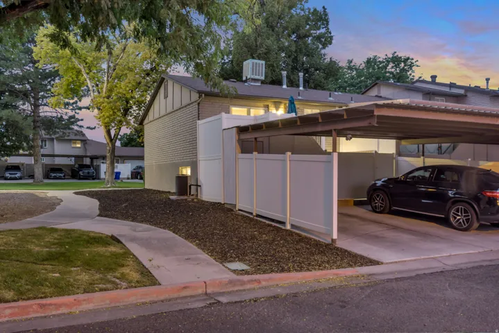 Carport parking with a metal roof and concrete pad, complemented by a privacy fence and a paved pathway