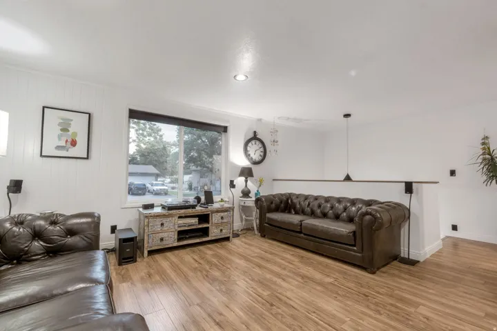 Living area featuring wood-finish flooring, white paneling, white walls, a large window, and recessed lighting