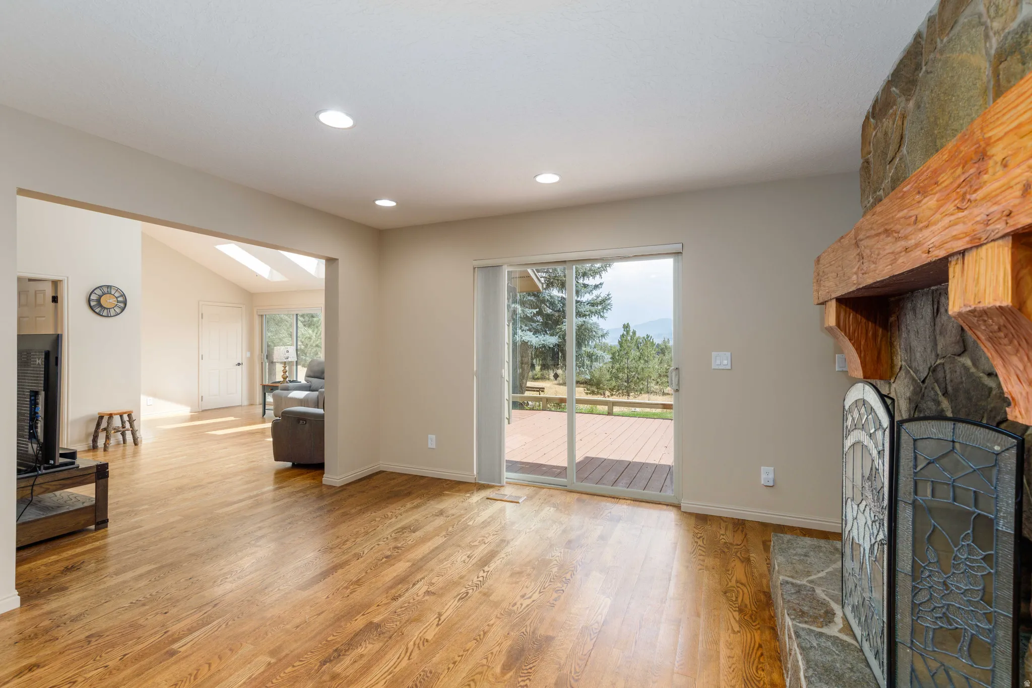Stone fireplace with a substantial wood mantel, wood-finish flooring, recessed lighting, and a sliding glass door to an outdoor deck