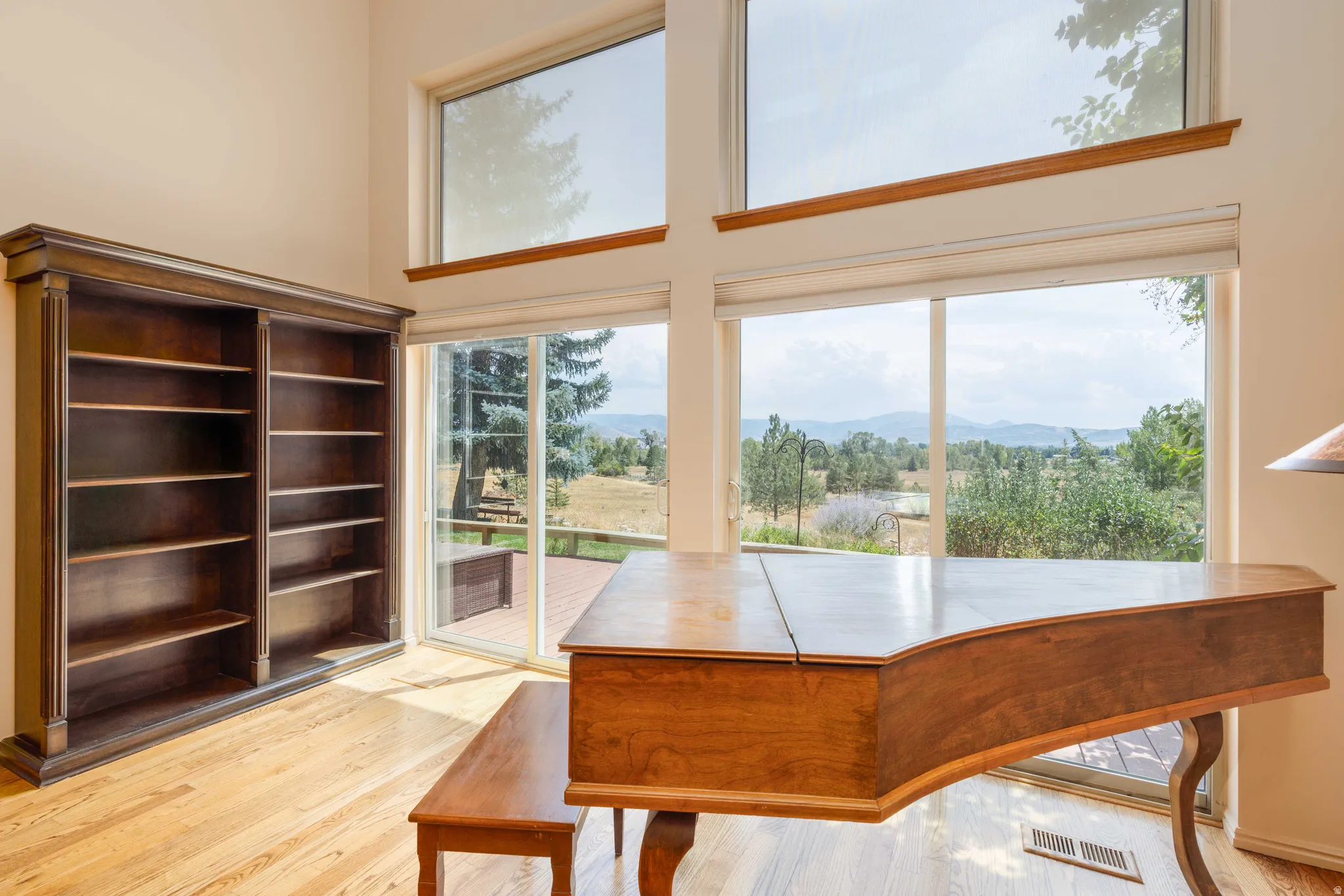 Vaulted ceiling with upper windows, light wood-finish flooring, built-in shelving, glass sliding door, and deck access
