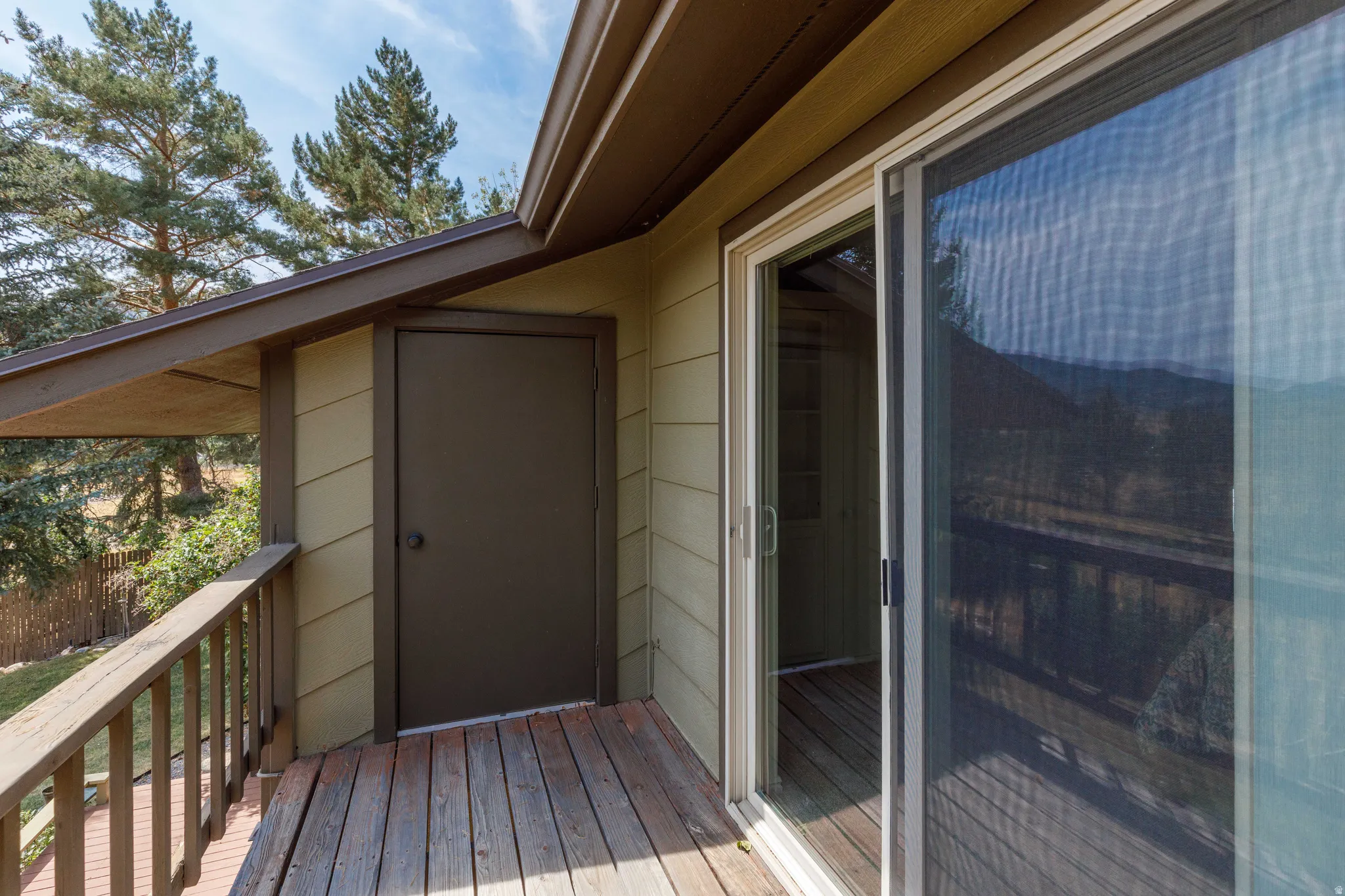 Wood-plank balcony featuring a wooden railing, sliding glass door with a screen, and an exterior storage door