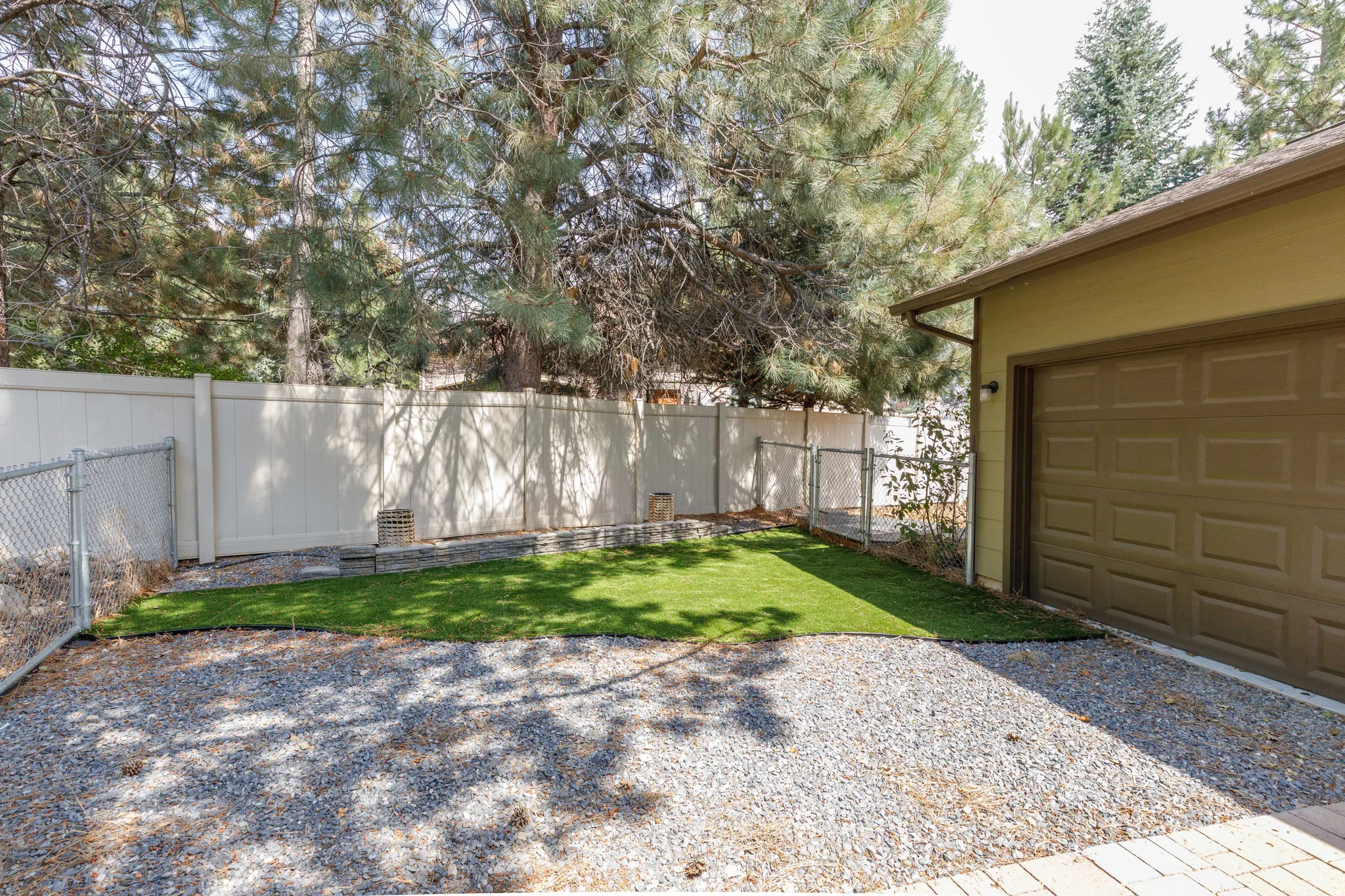 Fenced backyard area featuring artificial turf, gravel surfacing, and a paneled privacy fence