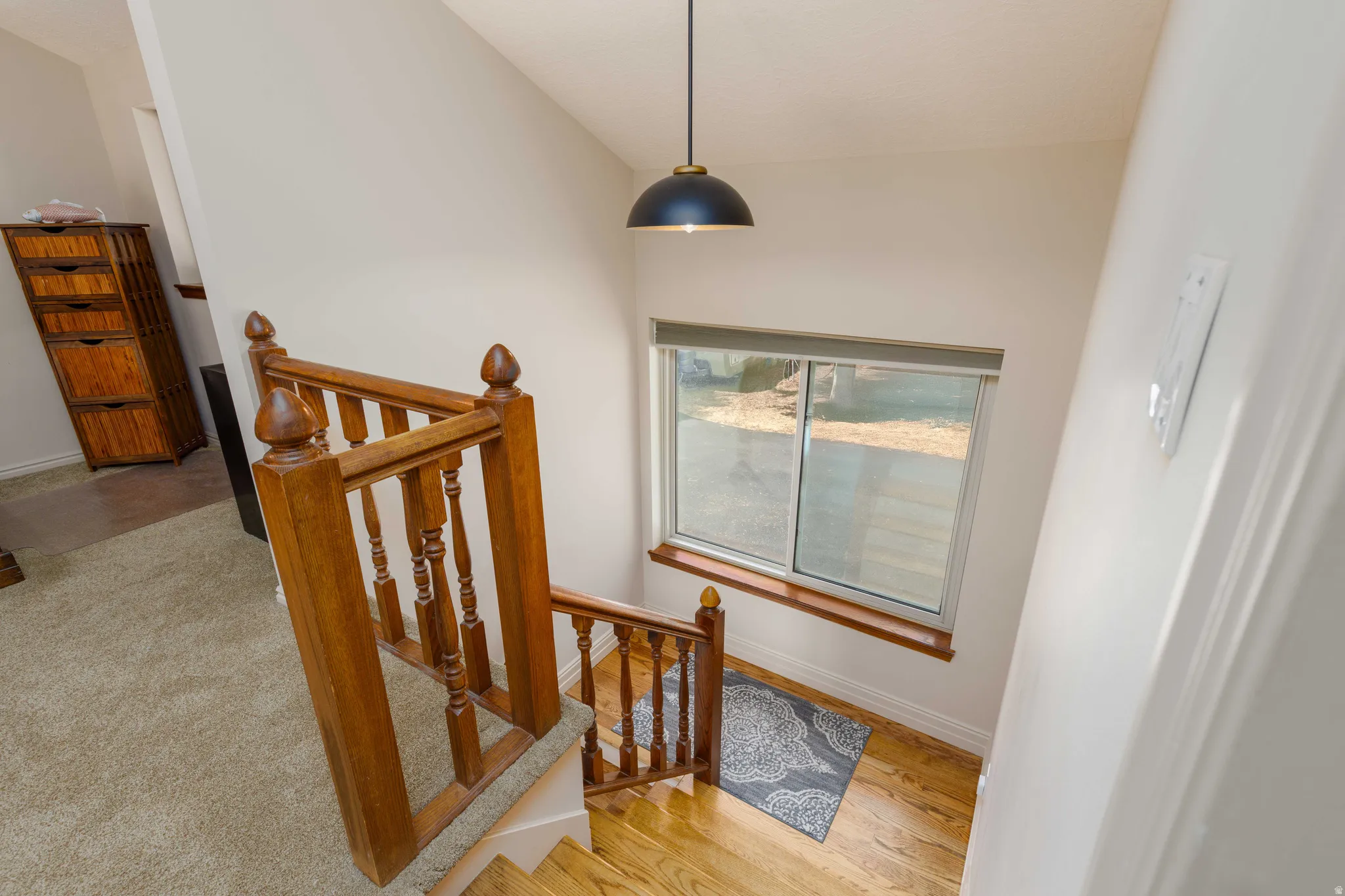 Wood-finish staircase with turned wood spindles and newel posts, complemented by a contemporary dome pendant light