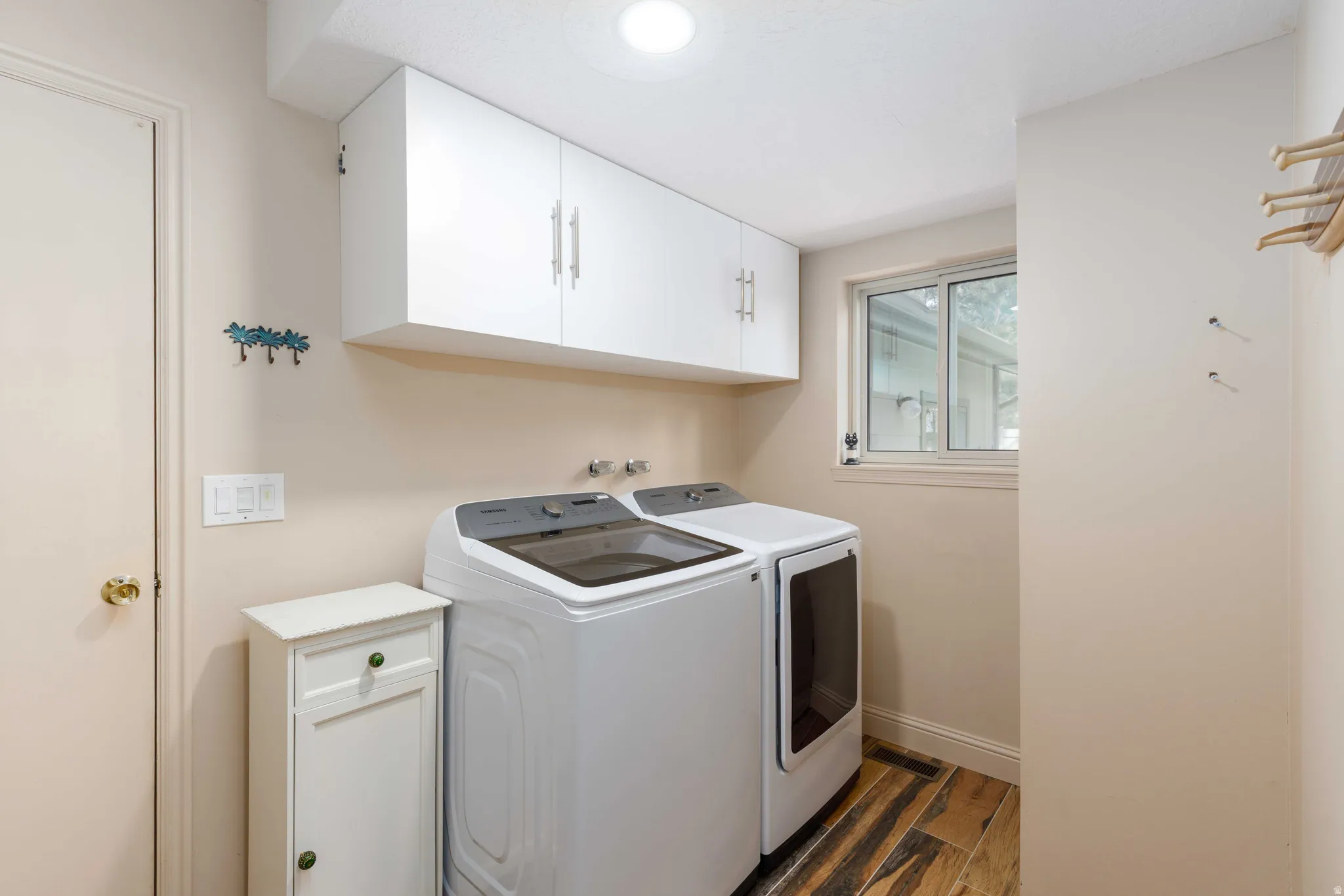 Wood-finish flooring, white overhead cabinetry with brushed nickel hardware, and a sliding window