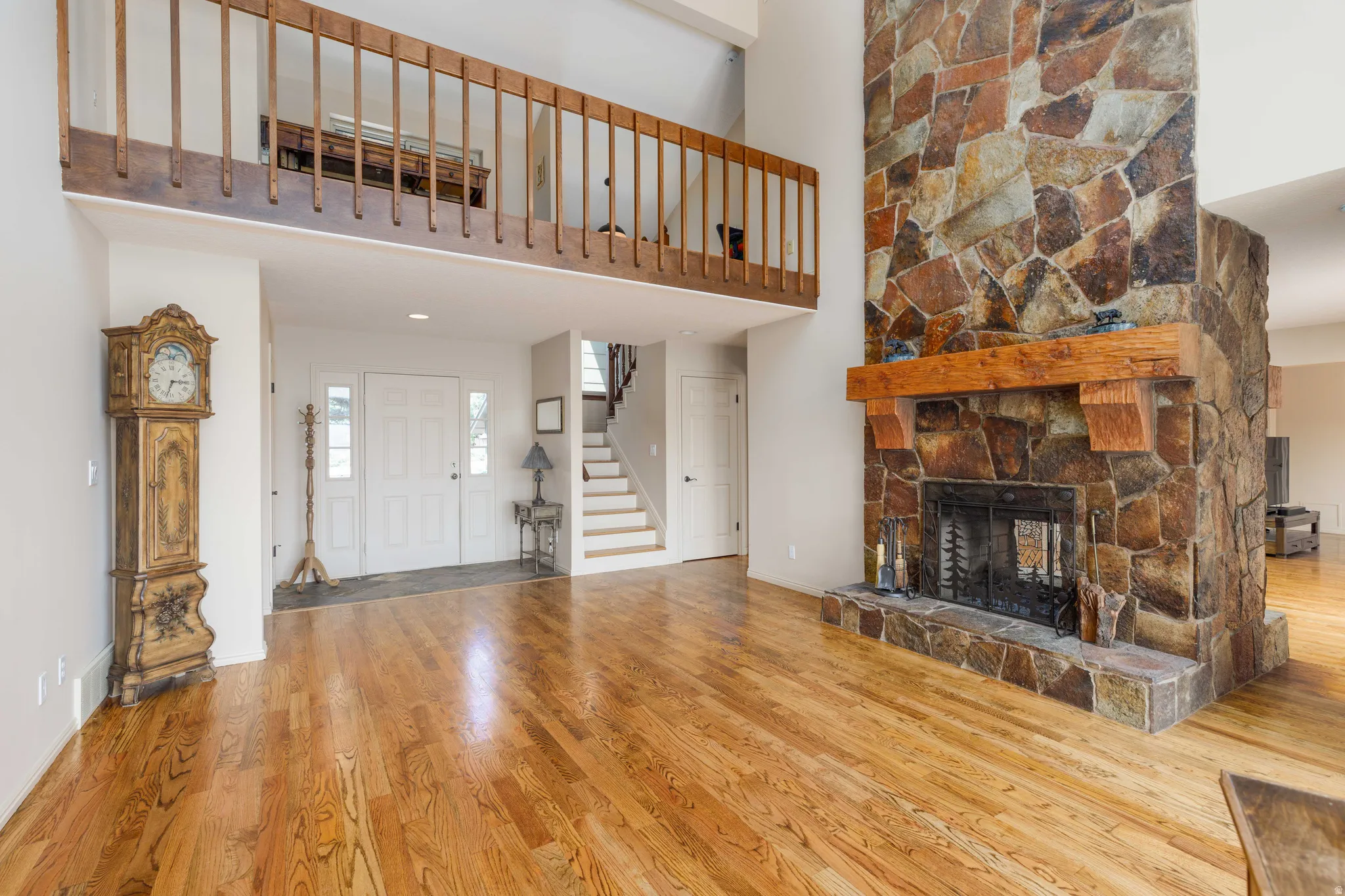 Hardwood flooring, stone fireplace with a substantial wood mantel, double-door entry, and an open balcony overlooking the space