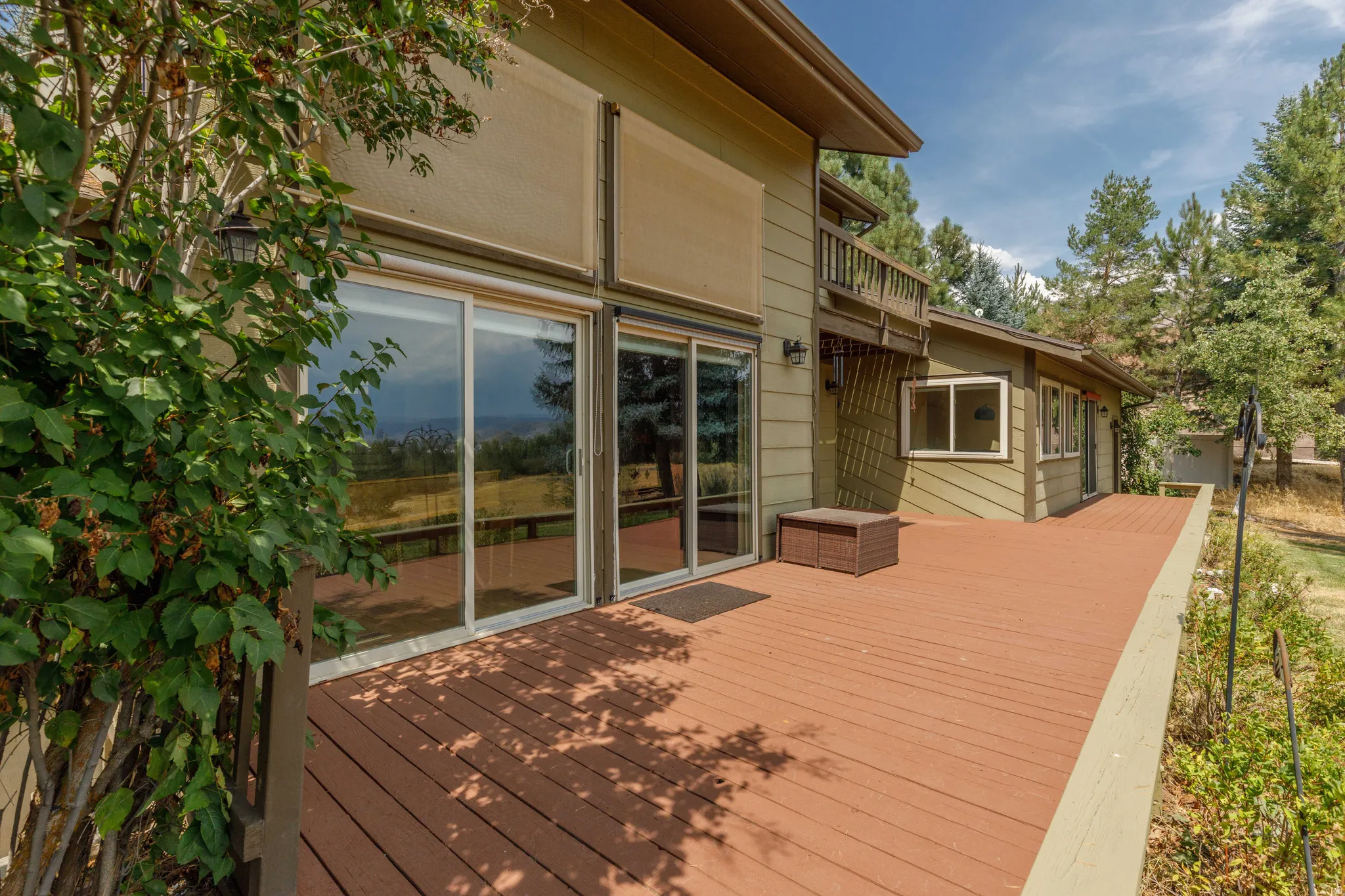 Expansive outdoor deck with a wood finish, multiple sliding glass doors, exterior wall lanterns, and a balcony above
