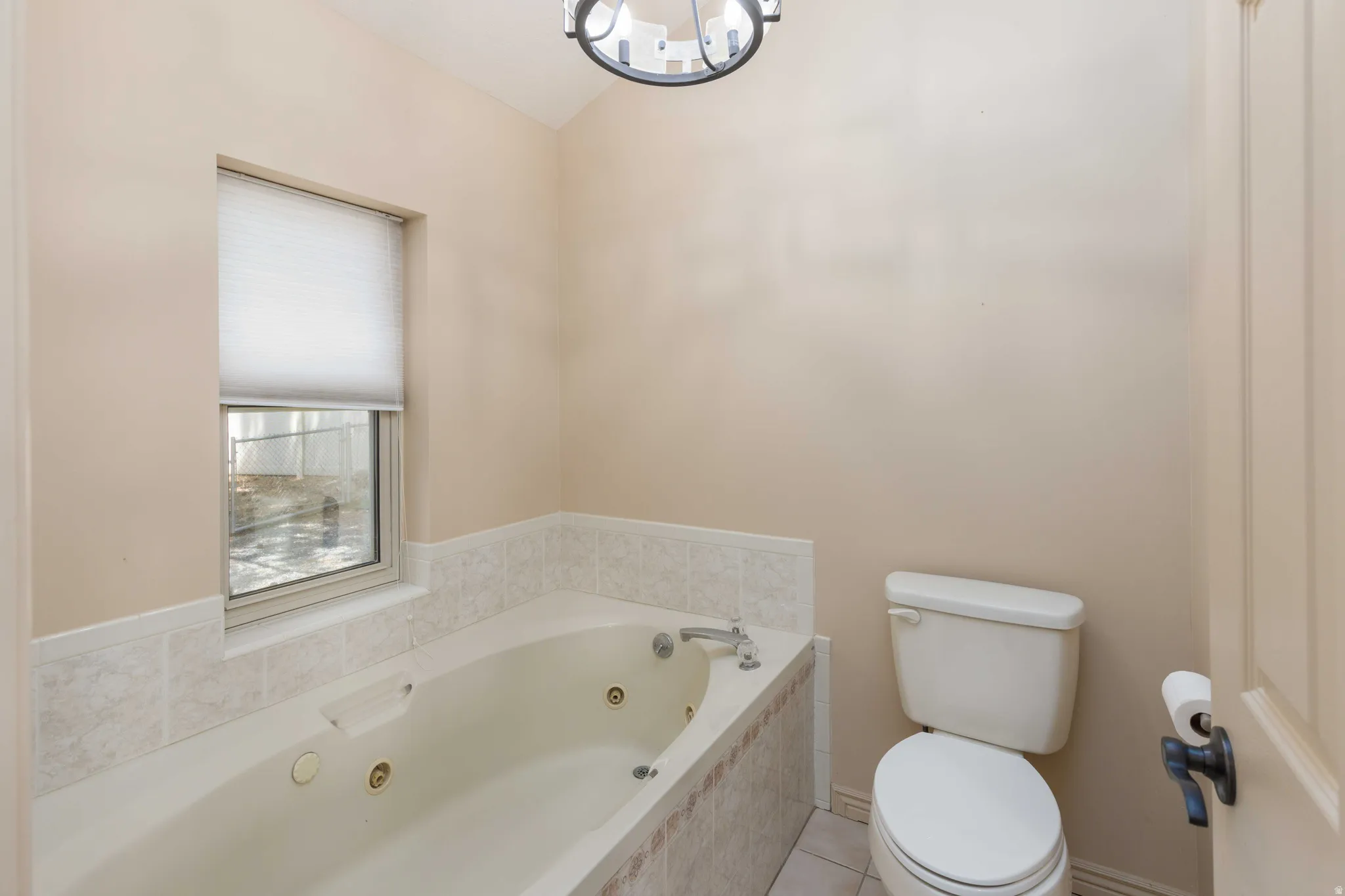 Built-in jetted tub with tiled surround, white toilet, and a window with a privacy shade