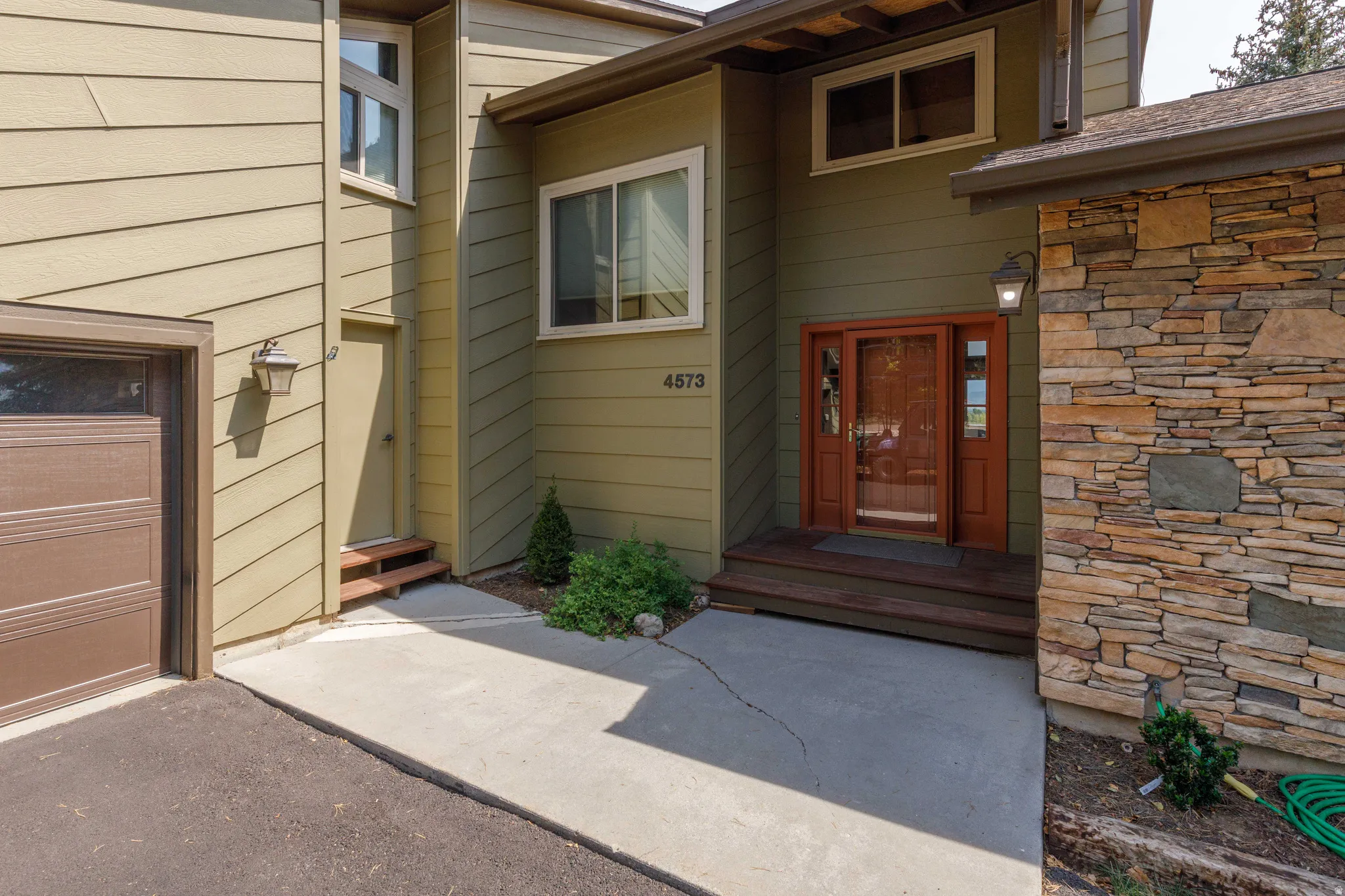 Siding exterior with stone veneer accents, an attached garage, a main entry with a wood-framed door, and a secondary entry with wood steps