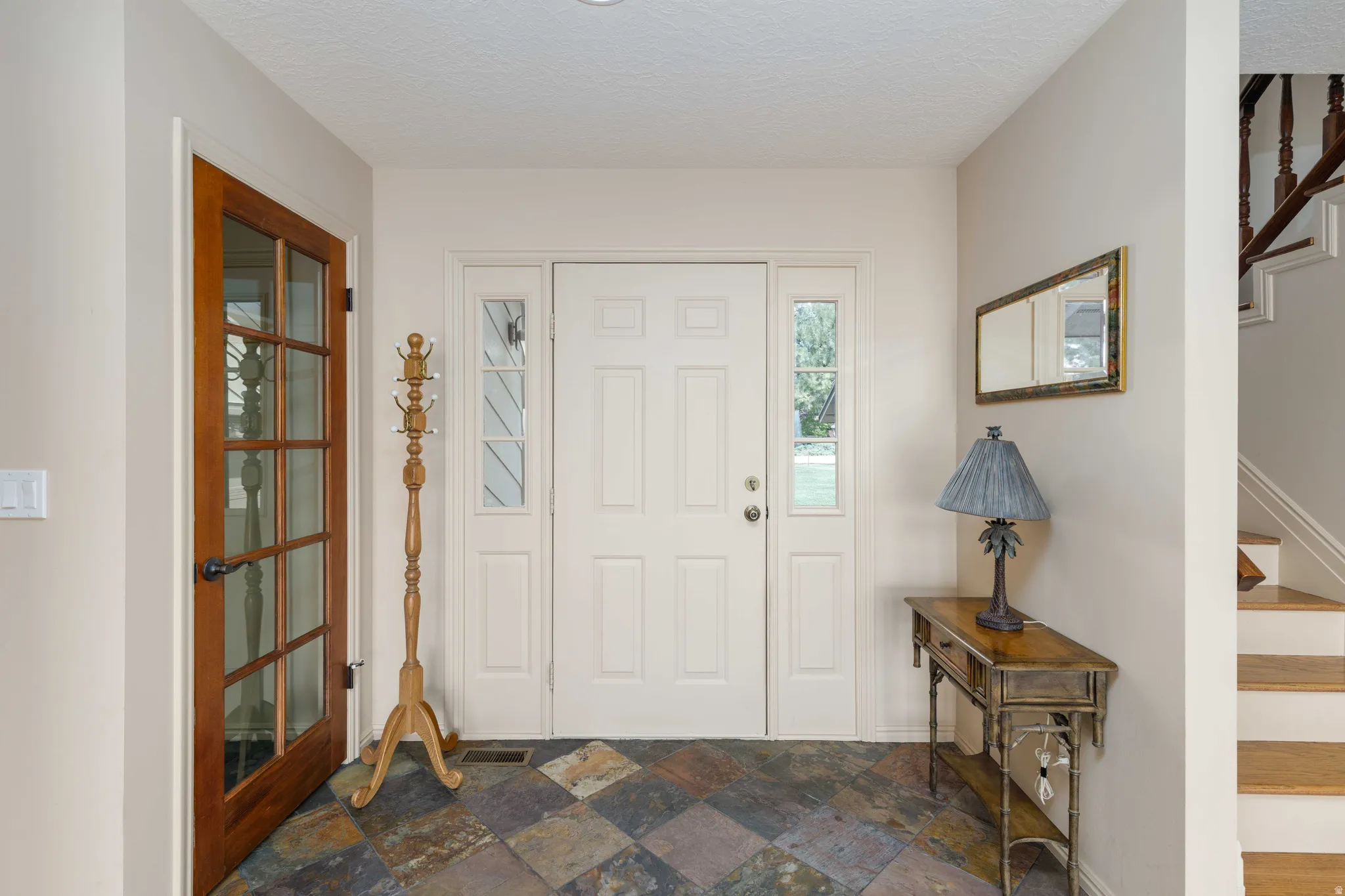 Entryway with multi-tone slate tile flooring, a white paneled front door with sidelights, and a wood-frame glass panel door