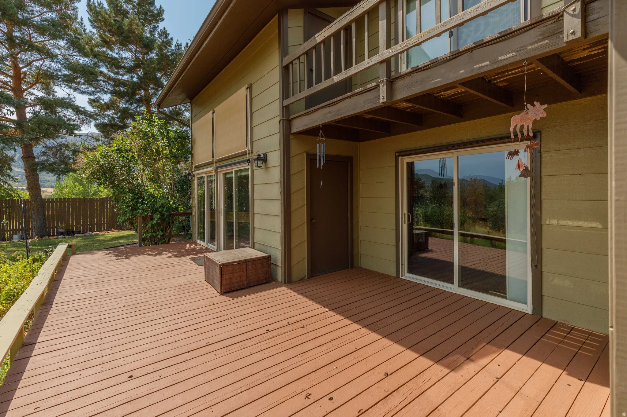 Expansive multi-level wood deck, neutral exterior siding, upper-level balcony, multiple glass sliding doors, and a natural landscape backdrop