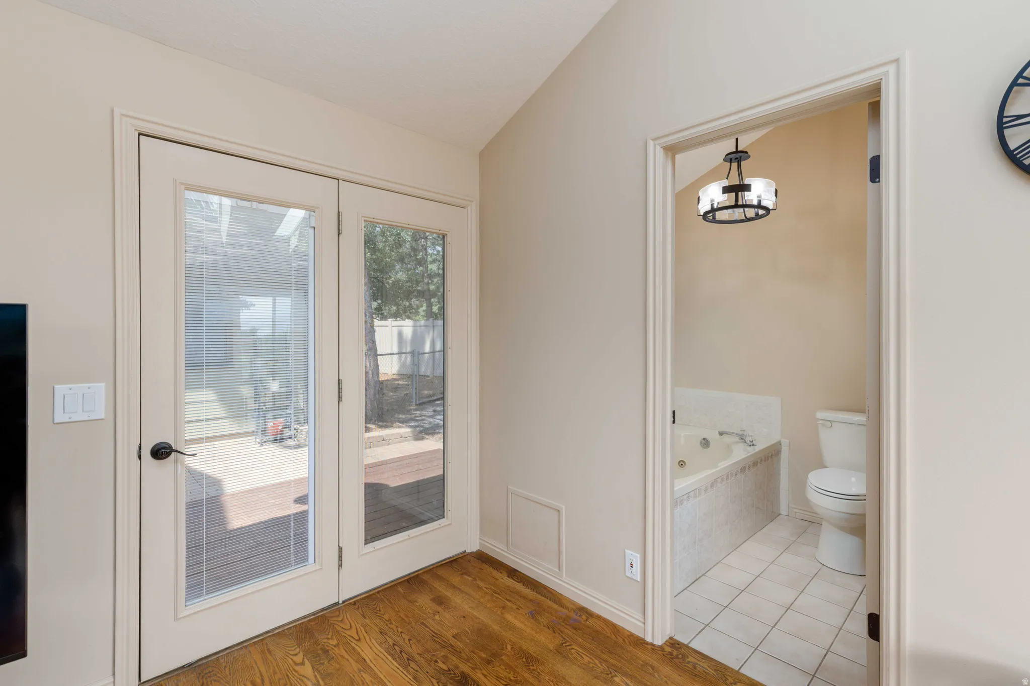 Wood-finish flooring, French doors with glass panes, and an adjacent bathroom with a built-in jetted tub and tile flooring
