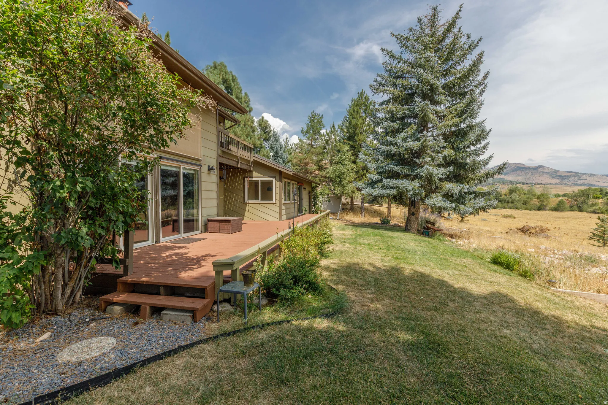 Expansive wood-finish deck with direct outdoor access, multiple sliding glass doors, and a terraced lawn area