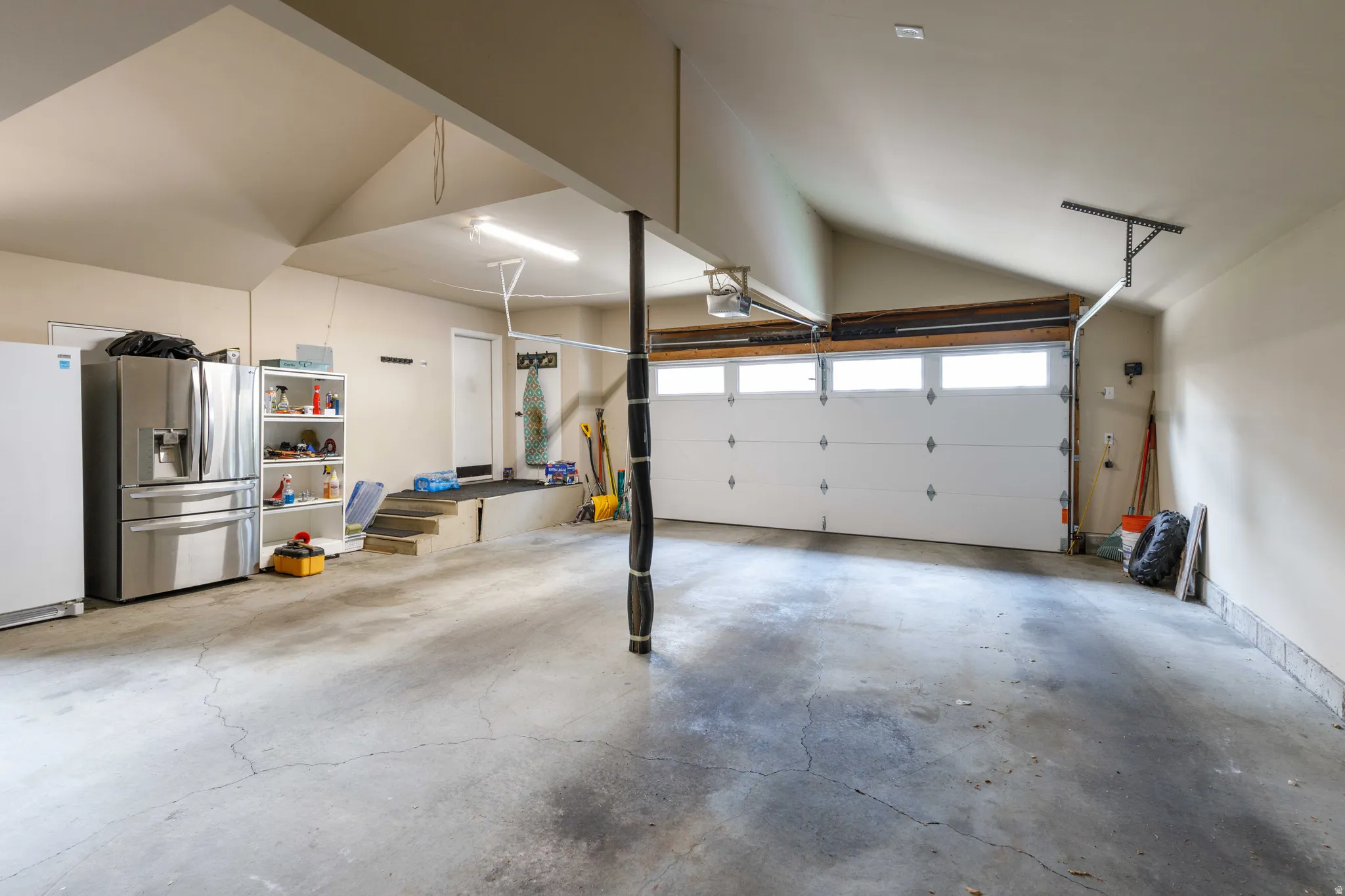 Spacious garage with an overhead door featuring upper window panels, vaulted ceiling, and concrete flooring