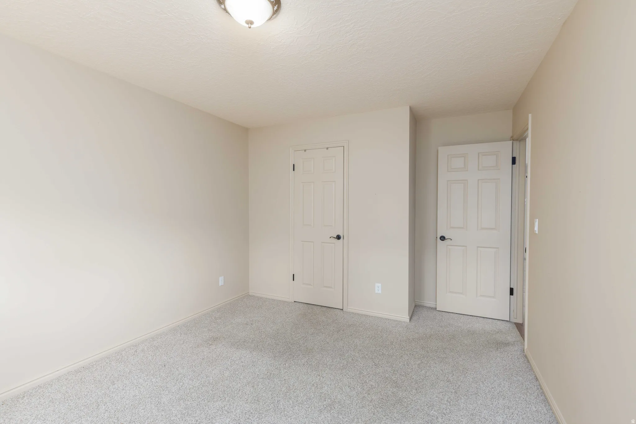 Neutral wall paint, textured ceiling, two paneled doors, carpet flooring, flush mount ceiling light fixture