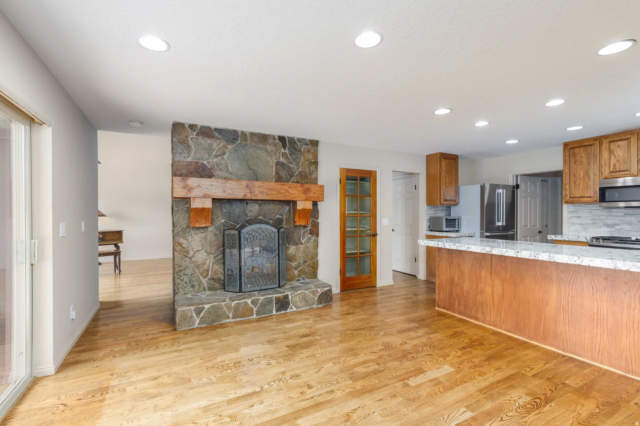 Stone-clad fireplace with a wood mantle, recessed lighting, wood-finish flooring, wood cabinetry, and a kitchen island with a stone countertop