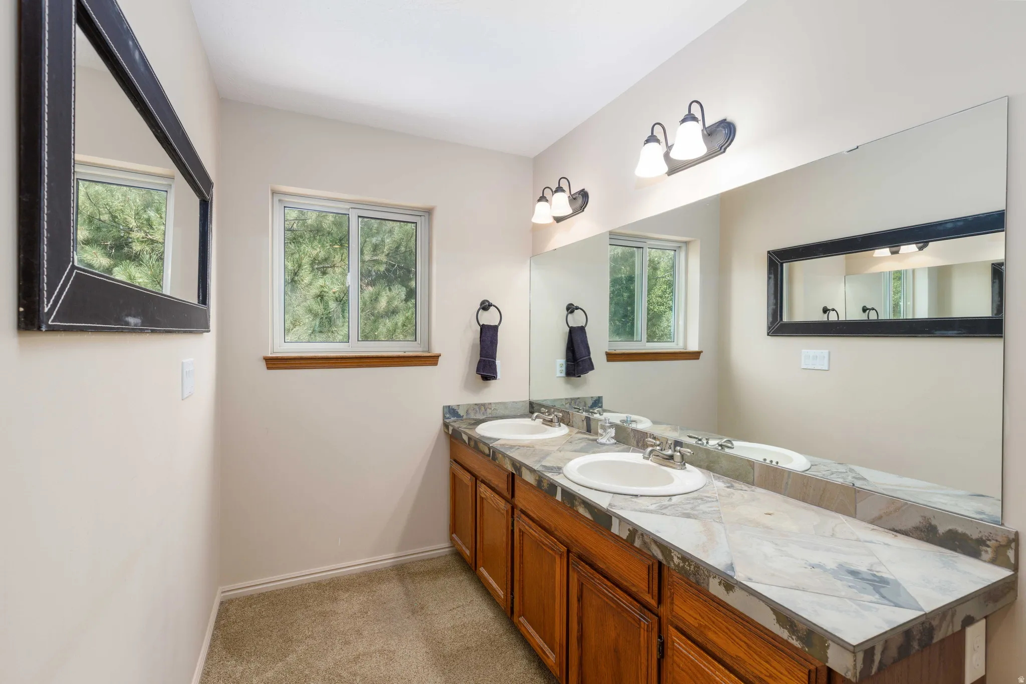 Dual vanity with integrated sinks, wood-finish cabinetry, tile countertop, and a large wall-mounted mirror