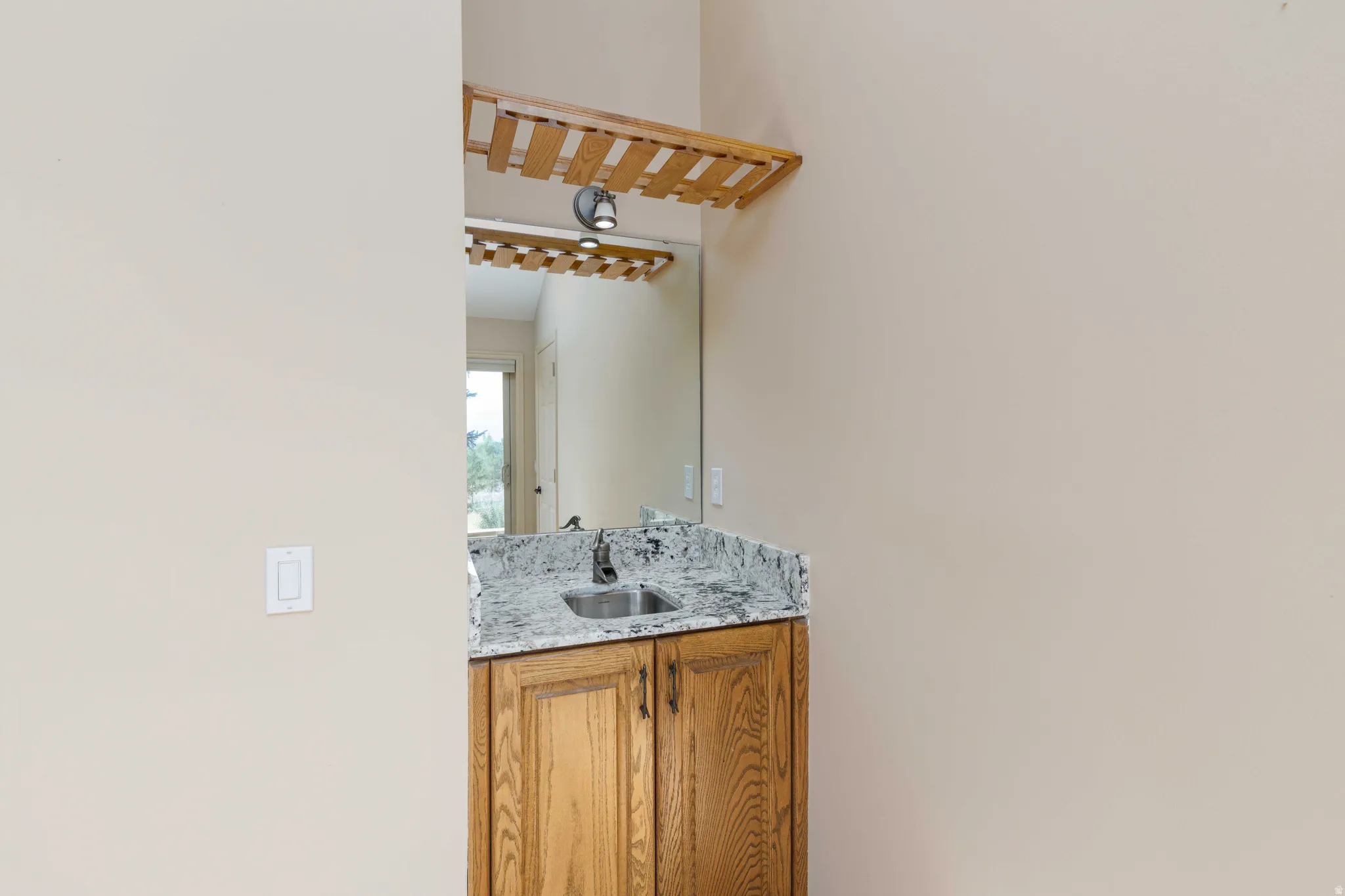 Built-in vanity with wood-finish cabinetry, granite countertop, undermount sink, and wall-mounted mirror