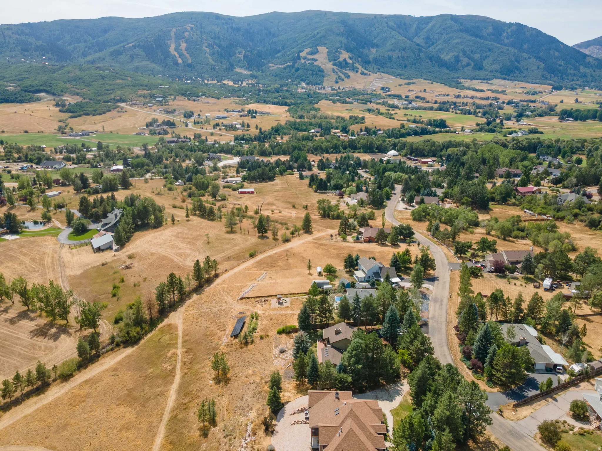 Expansive aerial perspective featuring a residential area, mature trees, and mountainous terrain