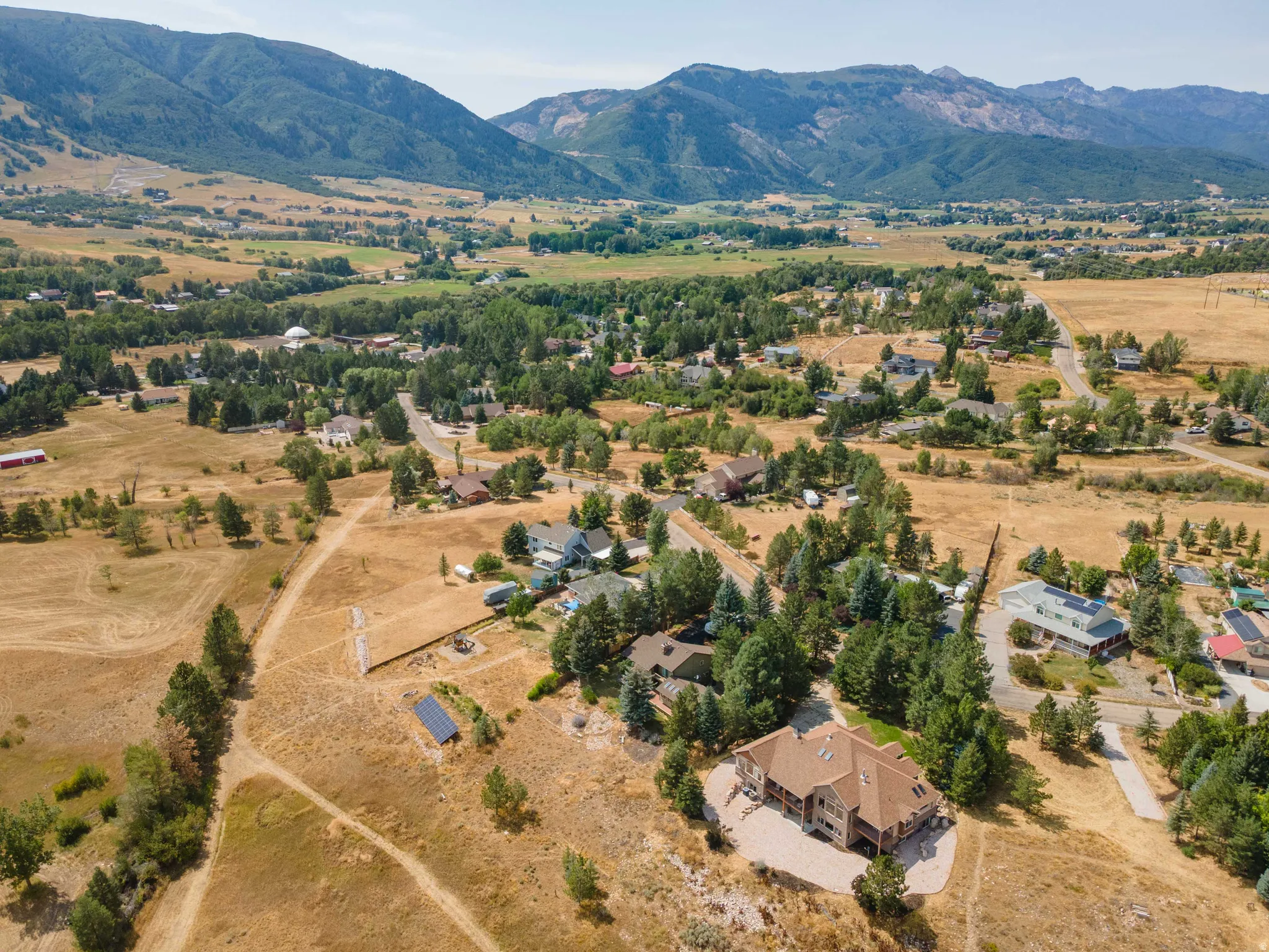Expansive property featuring a multi-level residence with a reddish-brown roof, mature trees, and mountainous surroundings