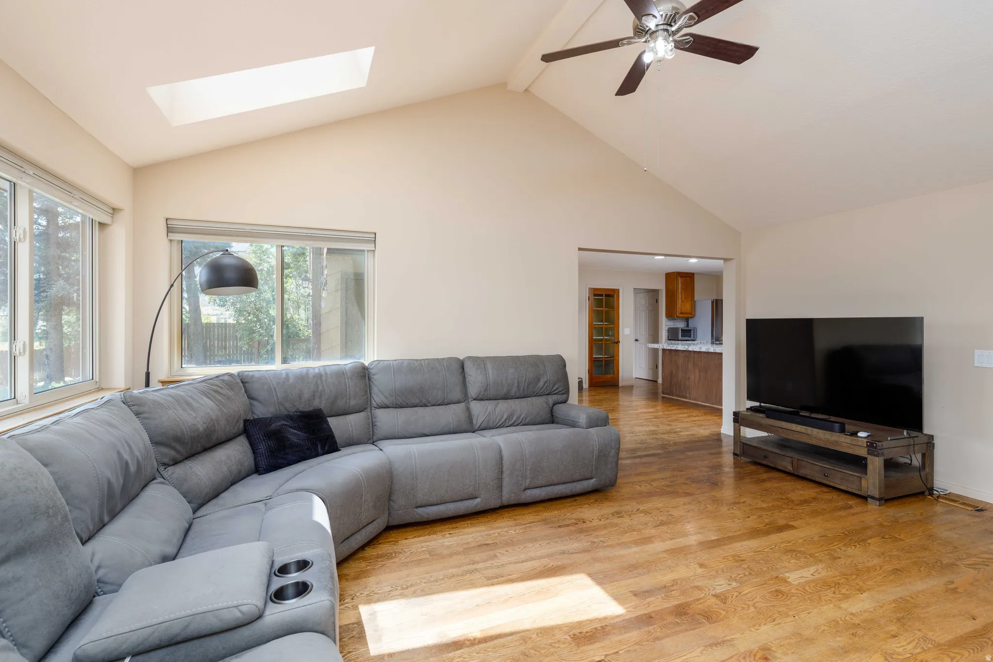Vaulted ceiling with a skylight and ceiling fan, wood-finish flooring, and multiple windows