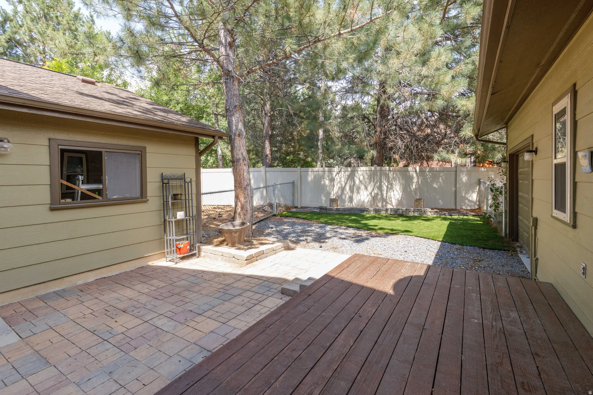 Spacious outdoor area featuring a wood deck, paver patio, gravel accents, and a section of green lawn