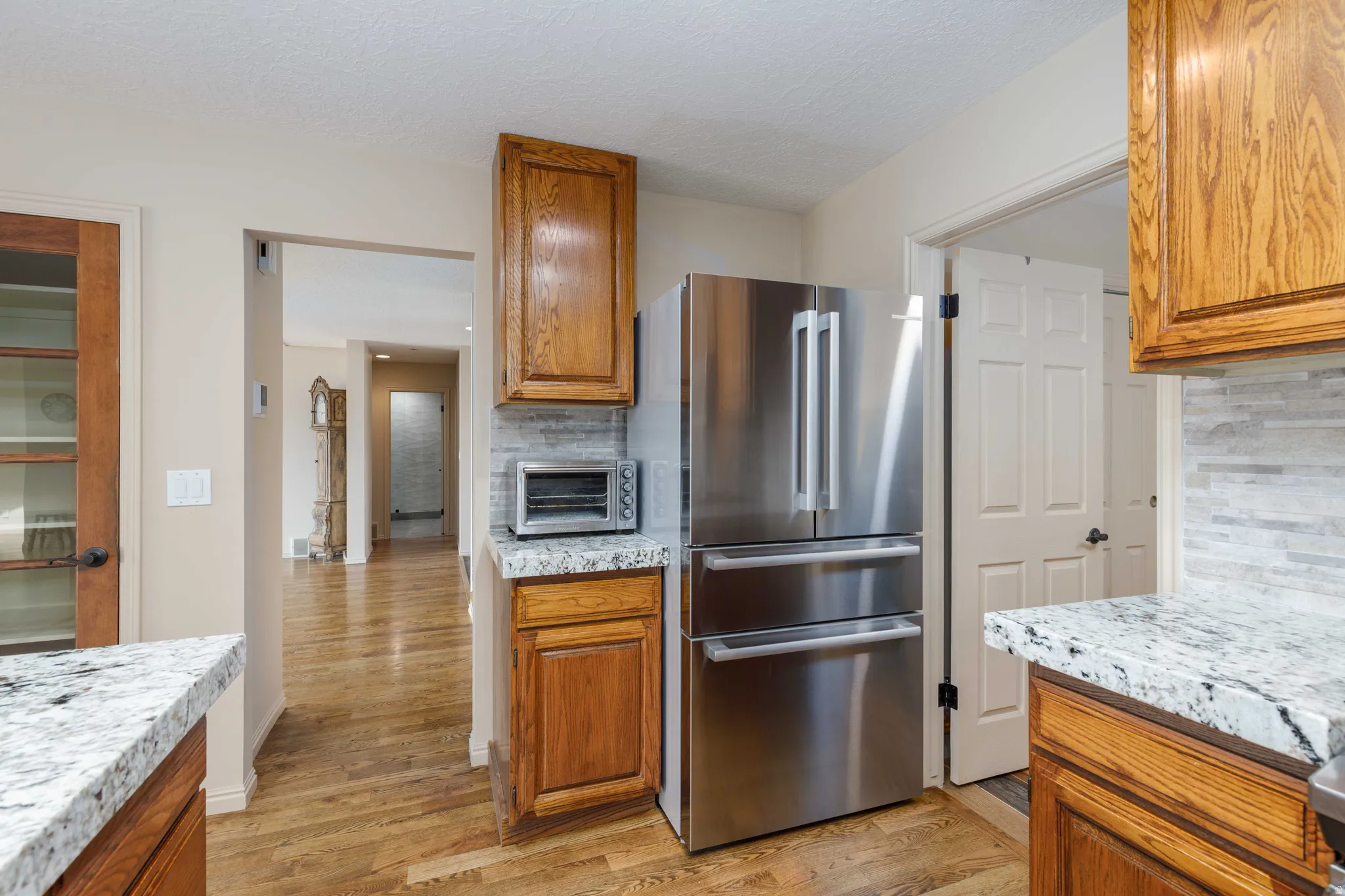 Stainless steel French door refrigerator, wood-finish flooring, light-toned cabinets, mosaic tile backsplash, and speckled countertops