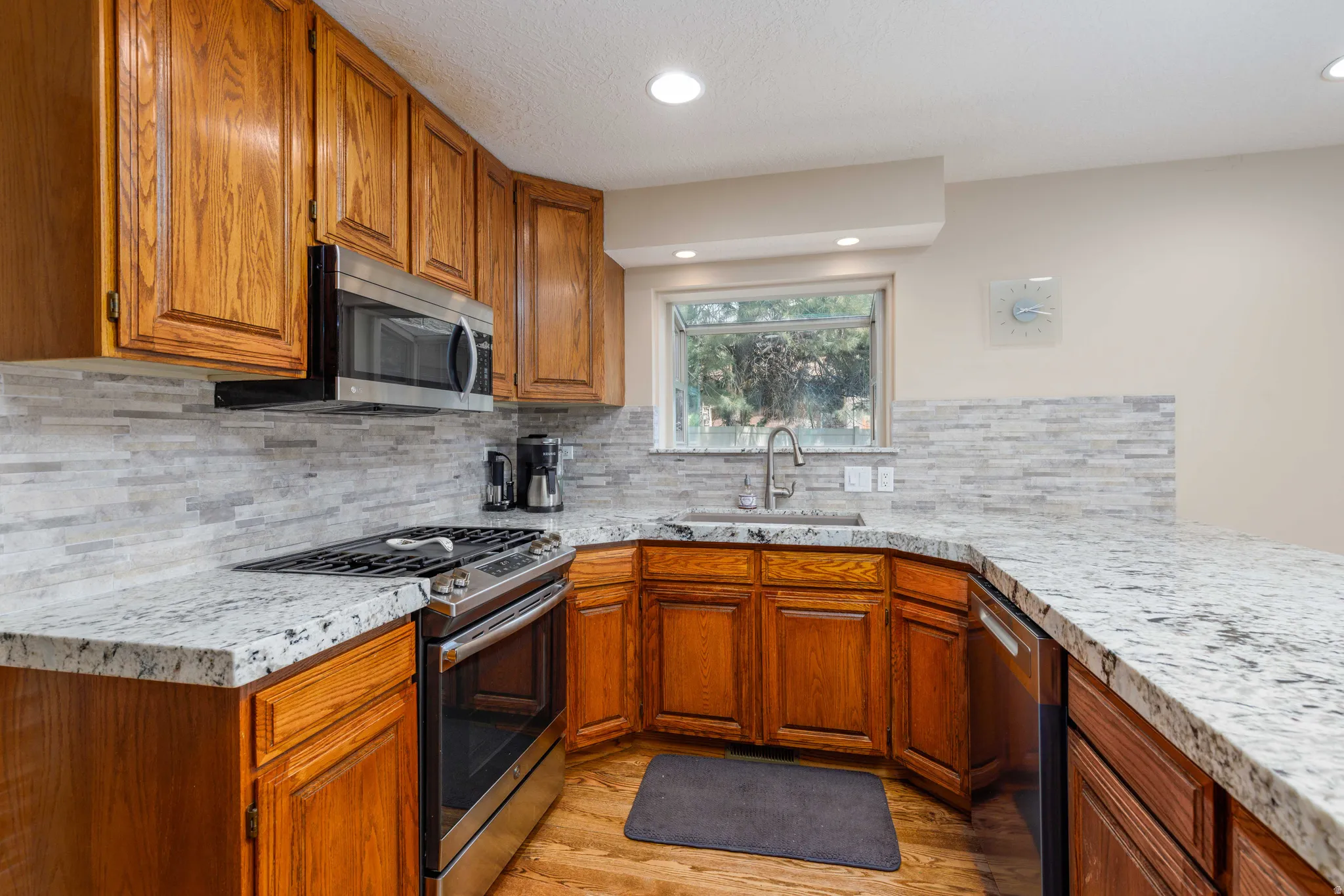 Kitchen featuring wood cabinetry, stainless steel appliances, a tiled backsplash, a stainless steel sink, and light-colored countertops