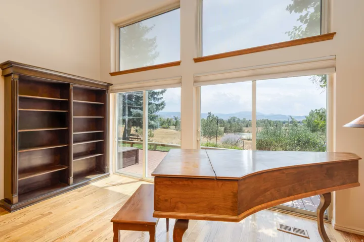 Vaulted ceiling with upper windows, light wood-finish flooring, built-in shelving, glass sliding door, and deck access