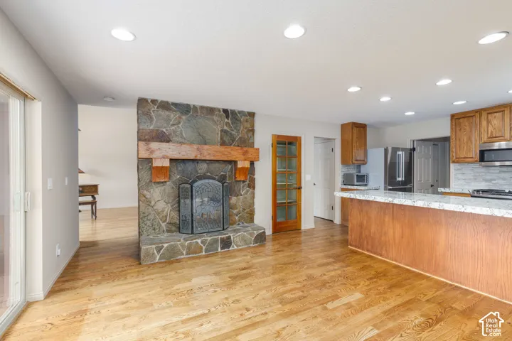 Stone-clad fireplace with a wood mantle, recessed lighting, wood-finish flooring, wood cabinetry, and a kitchen island with a stone countertop