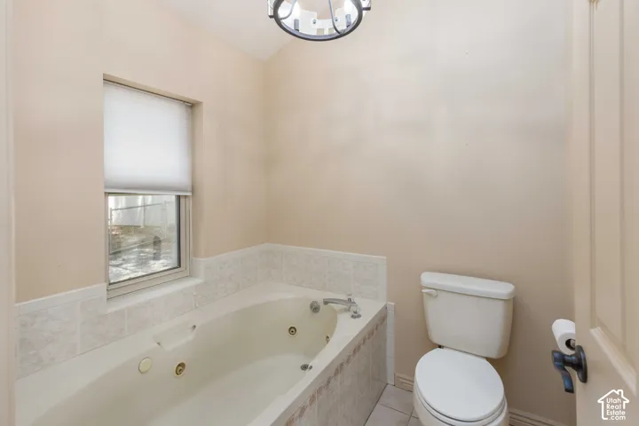 Built-in jetted tub with tiled surround, white toilet, and a window with a privacy shade