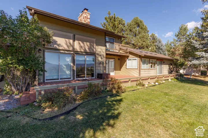 Multi-level exterior featuring a stone-faced chimney, expansive wood deck, second-story balcony, and large sliding glass doors