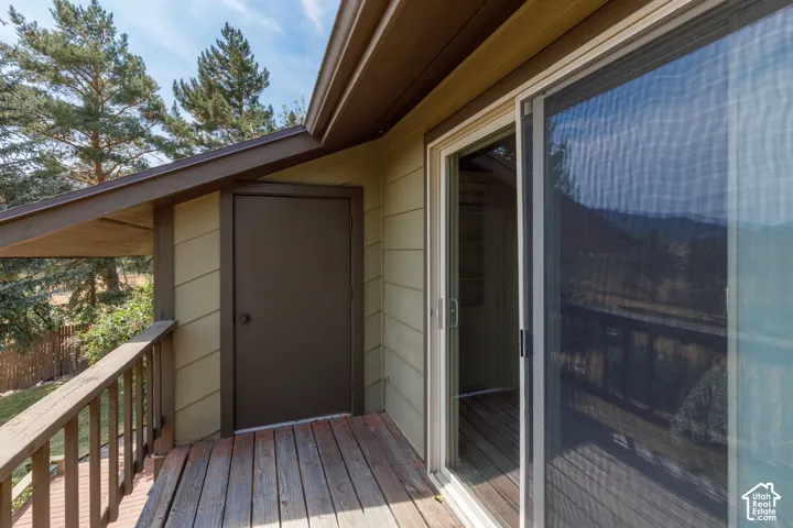Wood-plank balcony featuring a wooden railing, sliding glass door with a screen, and an exterior storage door