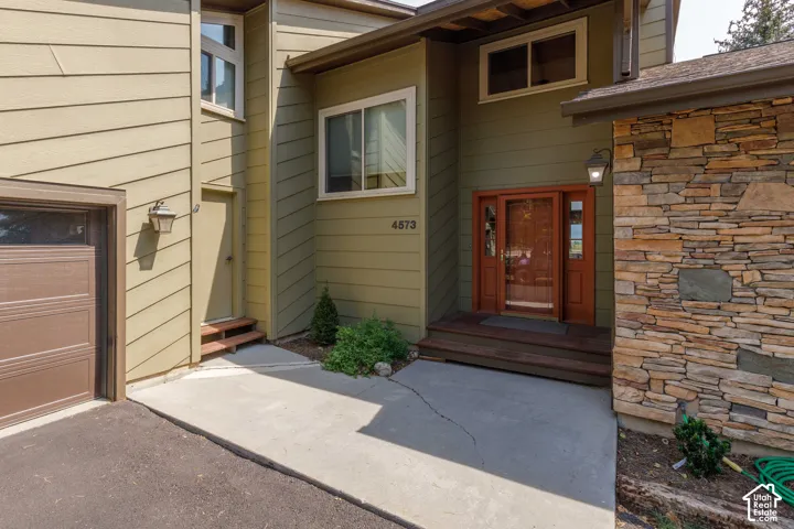 Siding exterior with stone veneer accents, an attached garage, a main entry with a wood-framed door, and a secondary entry with wood steps