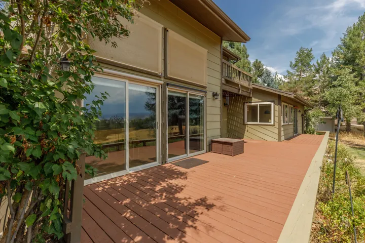Expansive outdoor deck with a wood finish, multiple sliding glass doors, exterior wall lanterns, and a balcony above