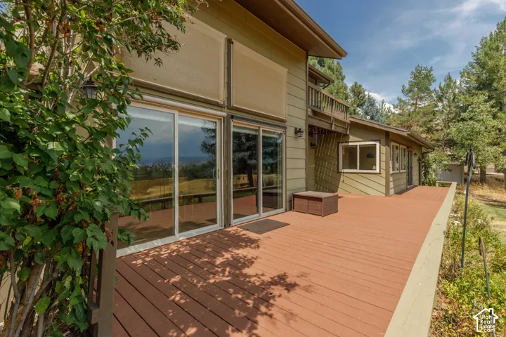 Expansive outdoor deck with a wood finish, multiple sliding glass doors, exterior wall lanterns, and a balcony above