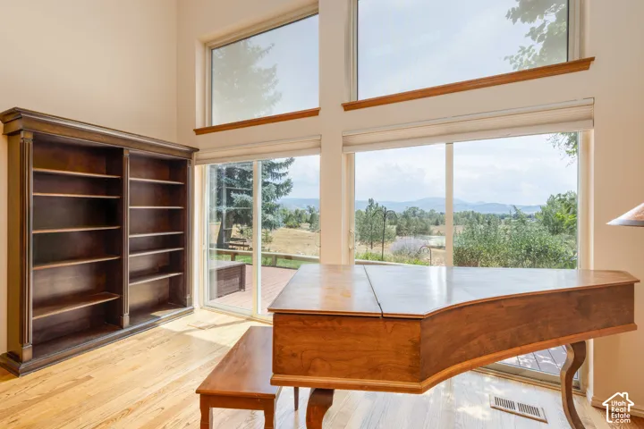 Vaulted ceiling with upper windows, light wood-finish flooring, built-in shelving, glass sliding door, and deck access