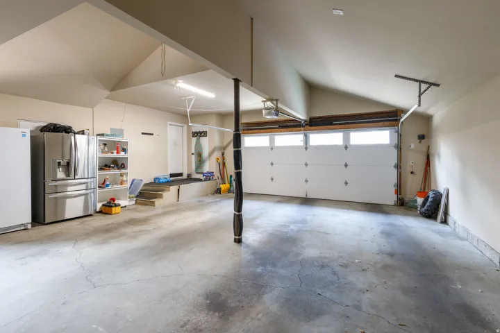 Spacious garage with an overhead door featuring upper window panels, vaulted ceiling, and concrete flooring