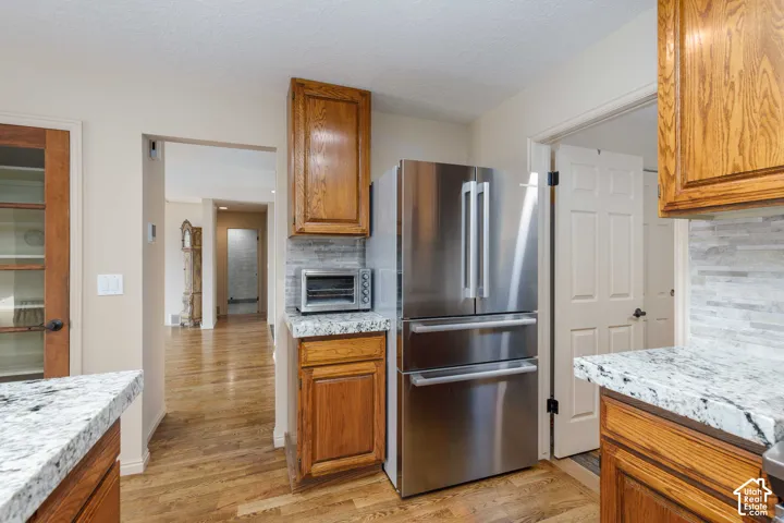 Stainless steel French door refrigerator, wood-finish flooring, light-toned cabinets, mosaic tile backsplash, and speckled countertops