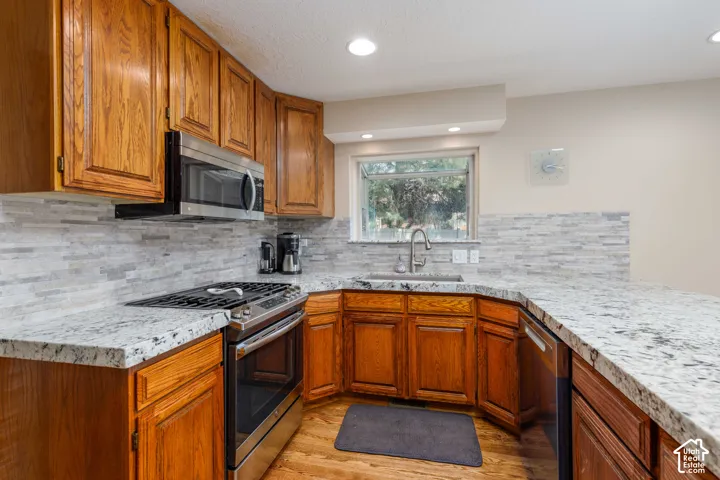 Kitchen featuring wood cabinetry, stainless steel appliances, a tiled backsplash, a stainless steel sink, and light-colored countertops