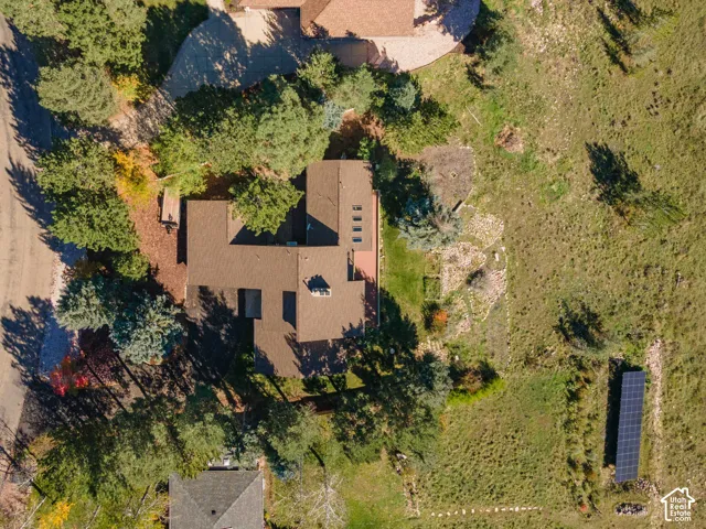 Aerial perspective of a multi-section residence featuring a composite roof, integrated skylights, a paved driveway, and a standalone solar panel array situated on a large, naturally landscaped lot