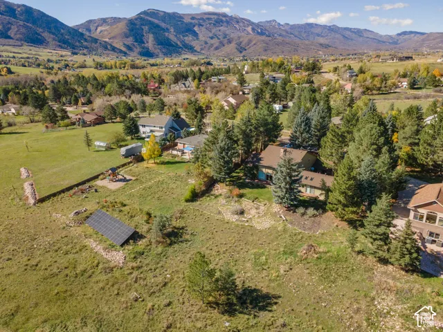 Aerial perspective featuring sprawling acreage, mature evergreen trees, ground-mounted solar panels, and mountainous terrain