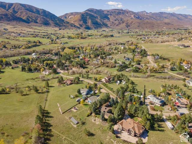 Aerial perspective of a multi-level residence on a large parcel featuring expansive mountain backdrops, mature evergreen trees, and surrounding open acreage