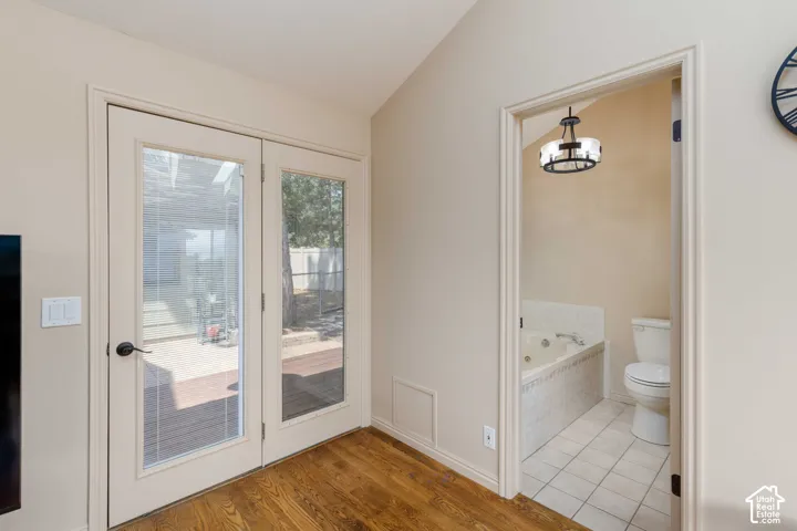 Wood-finish flooring, French doors with glass panes, and an adjacent bathroom with a built-in jetted tub and tile flooring