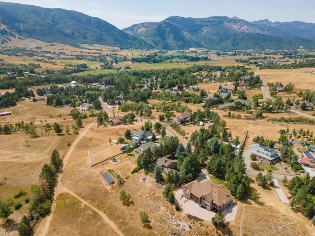 Expansive property featuring a multi-level residence with a reddish-brown roof, mature trees, and mountainous surroundings